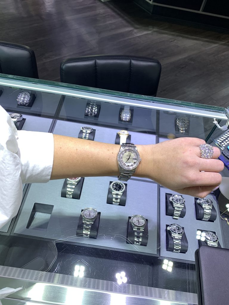 diamond rolex datejust watch worn in front of glass case with rolex watches at jewelry and watch store diamonds by raymond lee in boca raton, fl